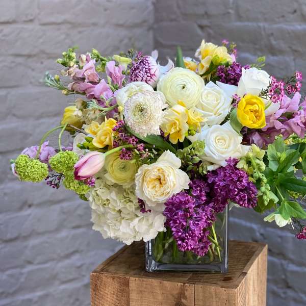 Mixed bouquet in a square glass vase with white, pink, yellow, and purple flowers