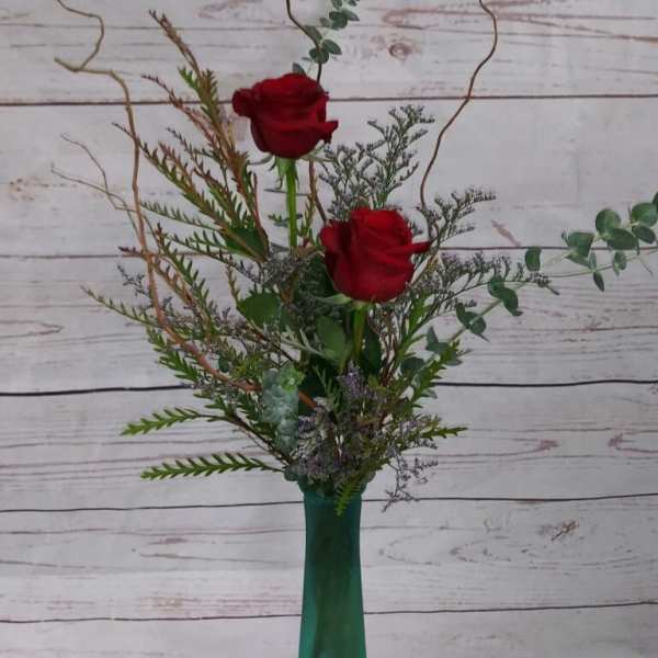 Two red roses in a tall green vase with airy greenery