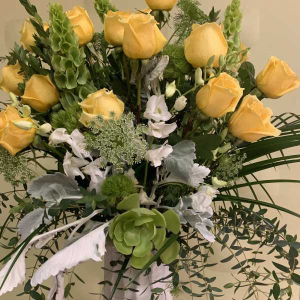Yellow roses and white flowers in a tall arrangement with cascading greenery