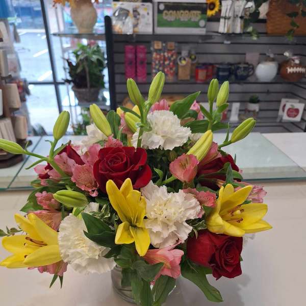Bouquet of red roses, yellow lilies, and white carnations in a glass vase