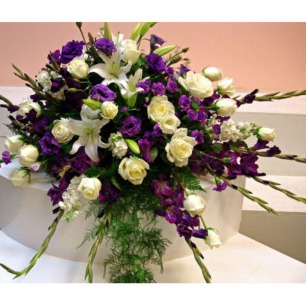Purple and white floral arrangement with roses and lilies on a white pedestal