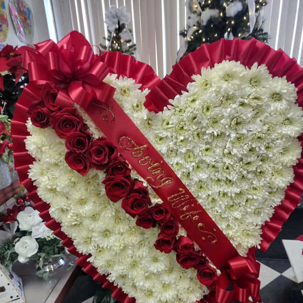 Heart-shaped floral arrangement with white daisies and red roses, wrapped in red ribbon.
