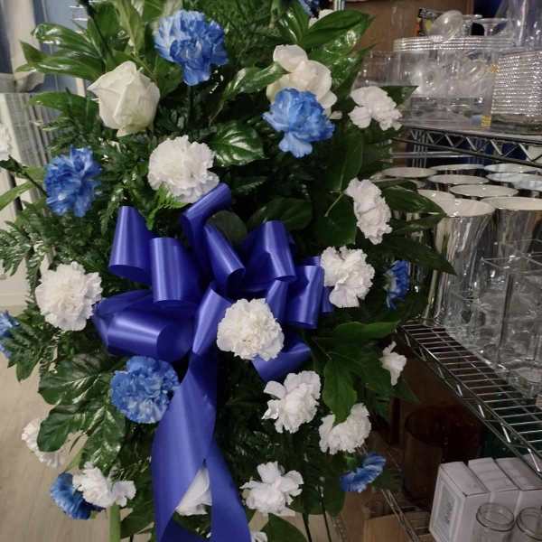 Standing floral spray with blue and white carnations and a purple ribbon