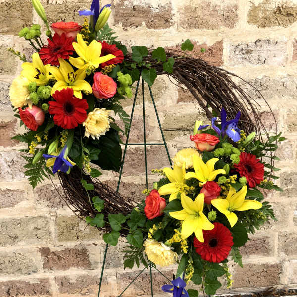Circular floral wreath with red, yellow, and pink blooms on a metal stand