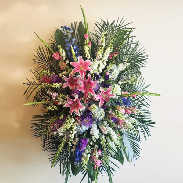 Large standing floral spray with pink lilies and mixed purple, white, and blue flowers