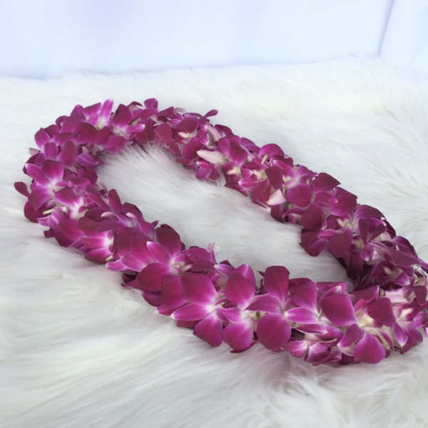 Purple orchid flower lei arranged in an oval on a white fur surface
