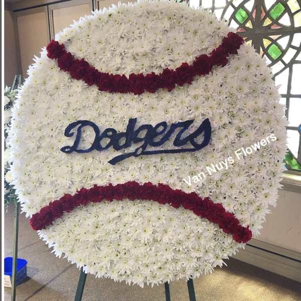 Large round baseball-shaped wreath of white flowers with red seams and blue Dodgers script on an easel.