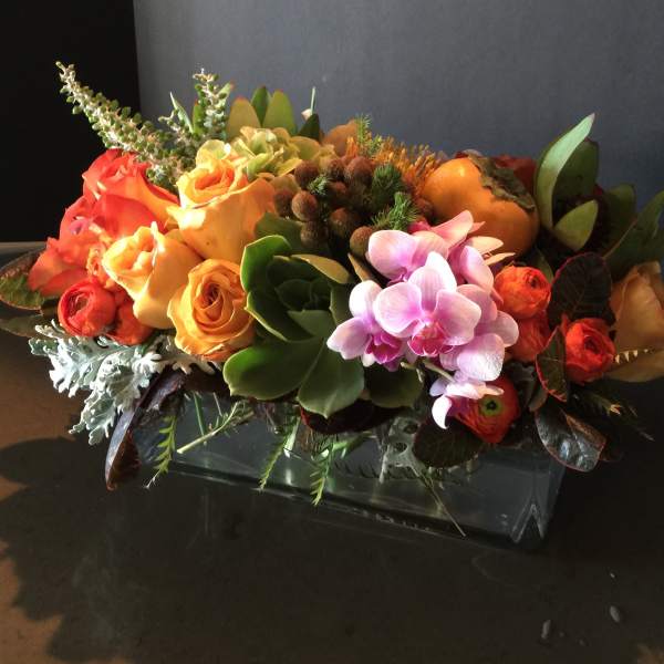 Orange roses and pink orchids in a low rectangular vase