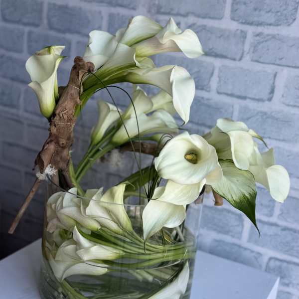 White calla lilies arranged in a glass vase with a branch accent