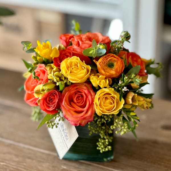 Bouquet of yellow, orange, and coral roses in a square glass vase
