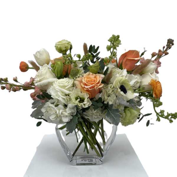 Mixed bouquet of white, peach, and orange flowers in a clear glass vase