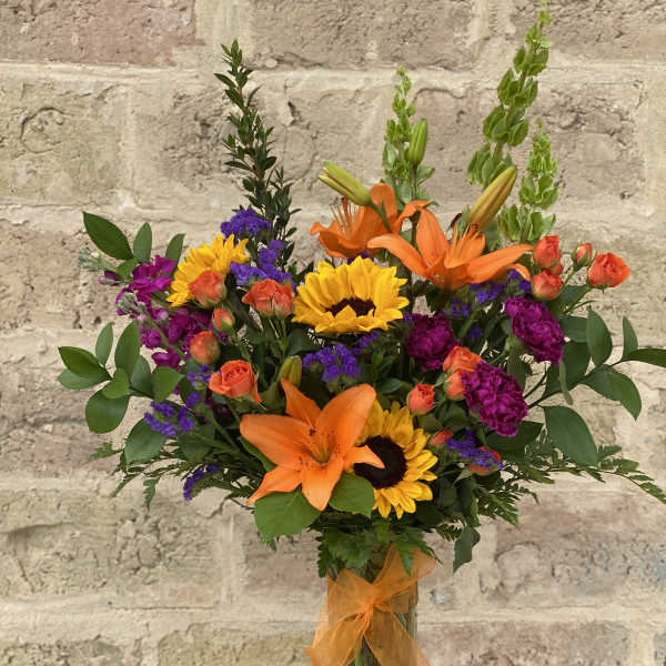 Bouquet of orange lilies, sunflowers, and purple flowers in a glass vase
