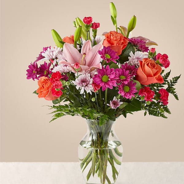 Mixed bouquet of pink lilies, roses, and daisies in a clear glass vase