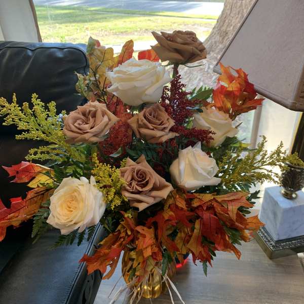 Bouquet of cream and tan roses with autumn leaves in a glass vase