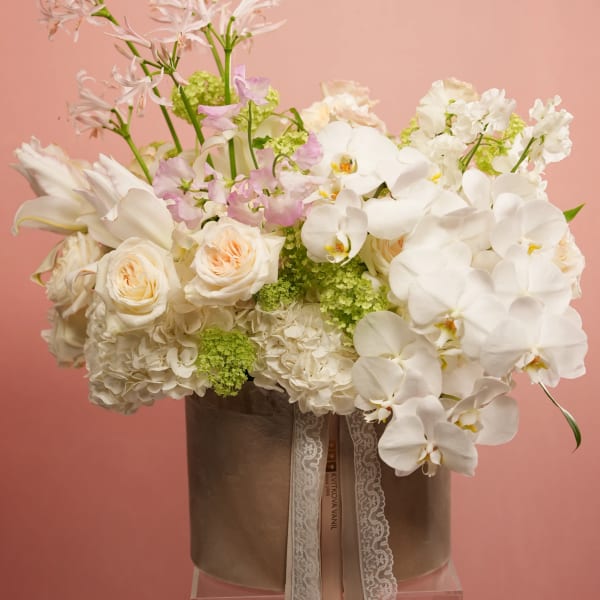 White orchids, roses, and hydrangeas arranged in a brown hatbox with lace ribbon.
