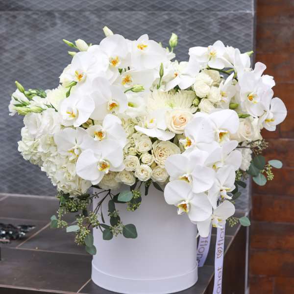 White orchids and roses arranged in a white hatbox