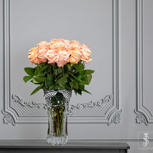Peach roses arranged in a clear glass vase with a striped ribbon.
