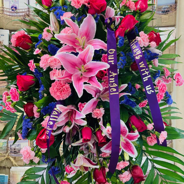 Large standing spray of pink lilies, red roses, and carnations with purple ribbons