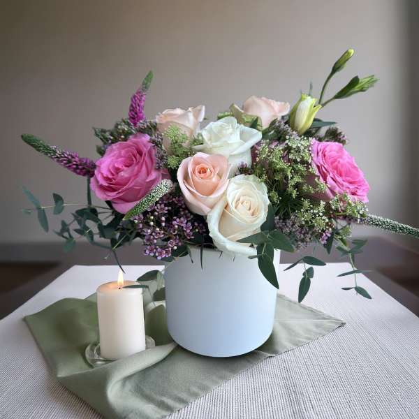 Pink and white roses in a white vase with a lit candle