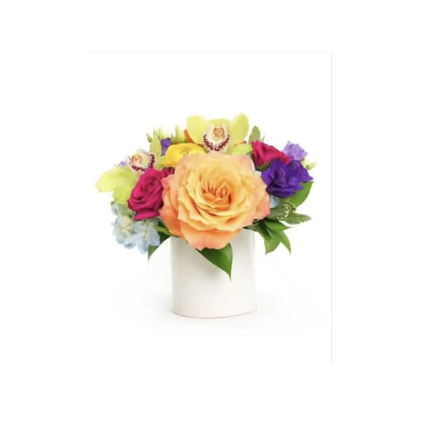 Colorful arrangement of peach roses, orchids, and mixed blooms in a white cylinder vase