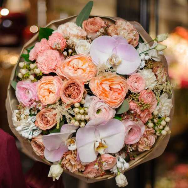 Bouquet of peach and pink flowers with pale orchids wrapped in brown paper