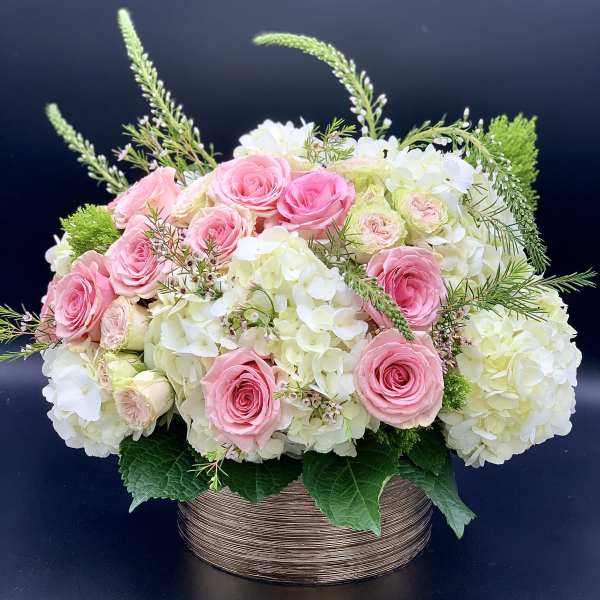 Pink roses and white hydrangeas in a round basket arrangement