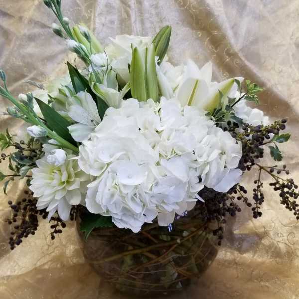 White floral arrangement in a round glass vase with lilies and hydrangeas