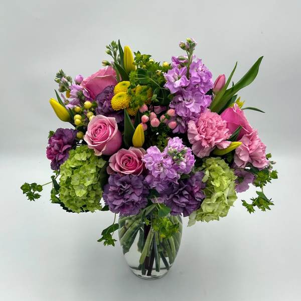 Mixed bouquet of pink, purple, and yellow flowers in a clear glass vase