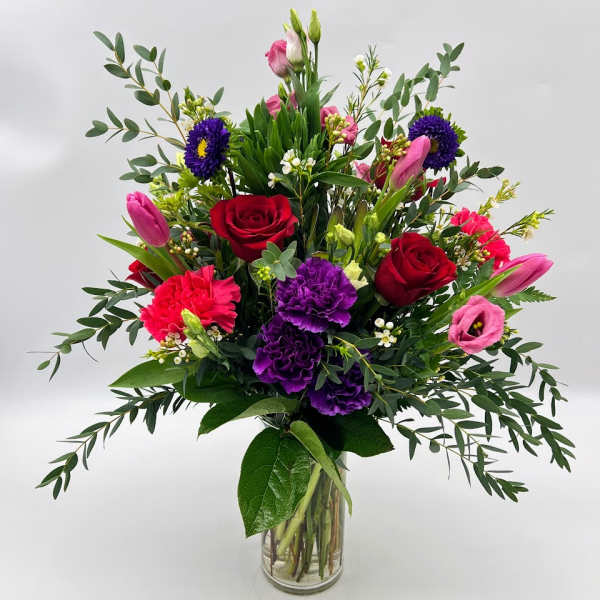 Mixed bouquet of roses, tulips, carnations, and purple blooms in a glass vase