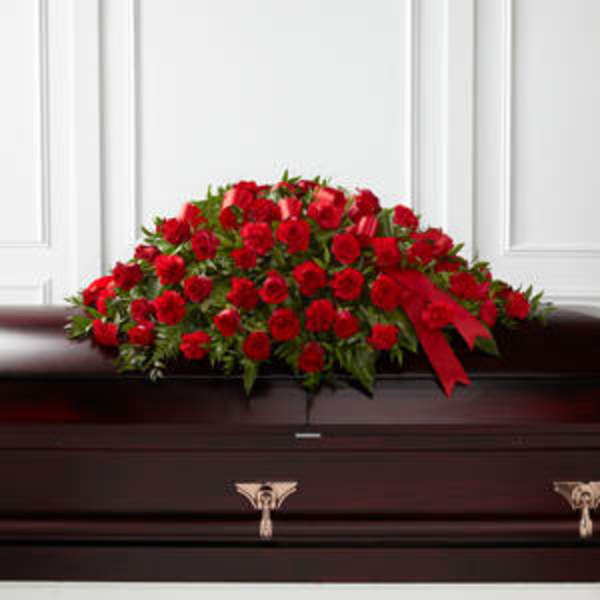 Red rose casket spray with a red ribbon on a dark casket