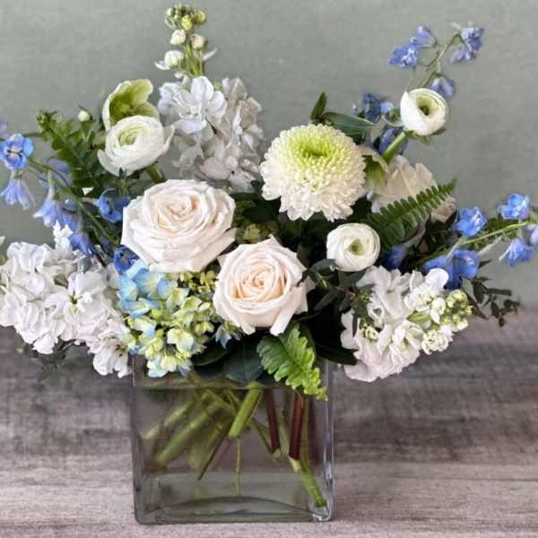 White and blue mixed flower arrangement in a square glass vase