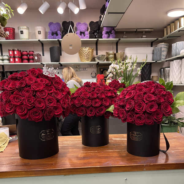 Three large red rose arrangements in black hat boxes on a counter