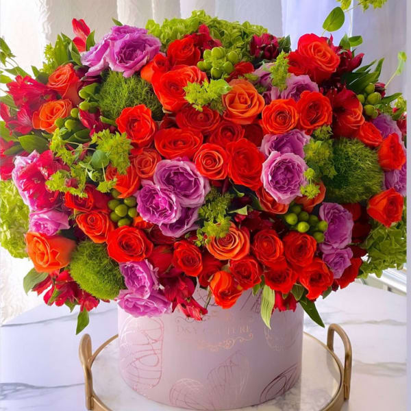 Large bouquet of red, orange, and purple roses in a pink round box