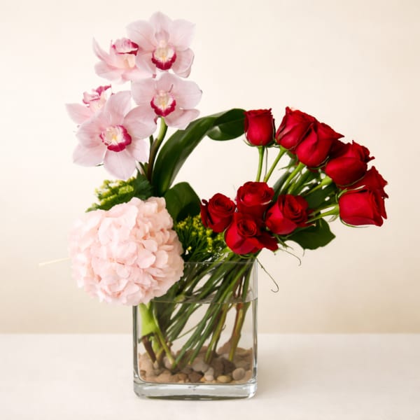 Pink orchids, red roses, and a pale pink hydrangea in a clear glass vase