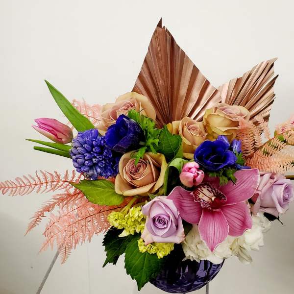 Bouquet of roses, orchids, and blue blooms in a purple vase