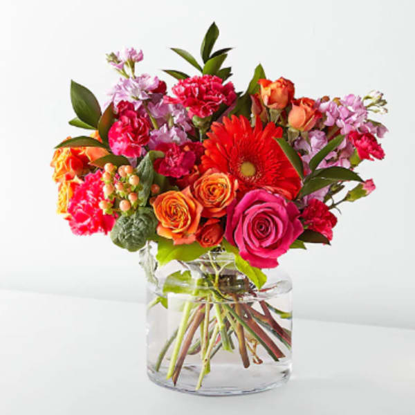 Mixed bouquet of roses, gerbera daisies, and carnations in a clear glass vase