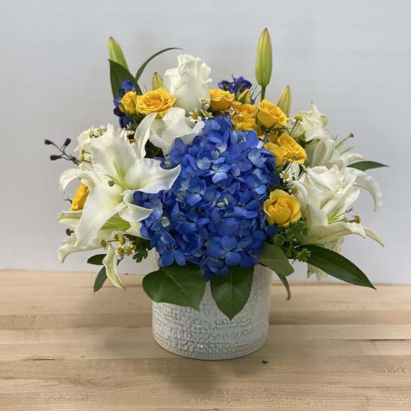 Blue hydrangea and white lilies with yellow roses in a white vase