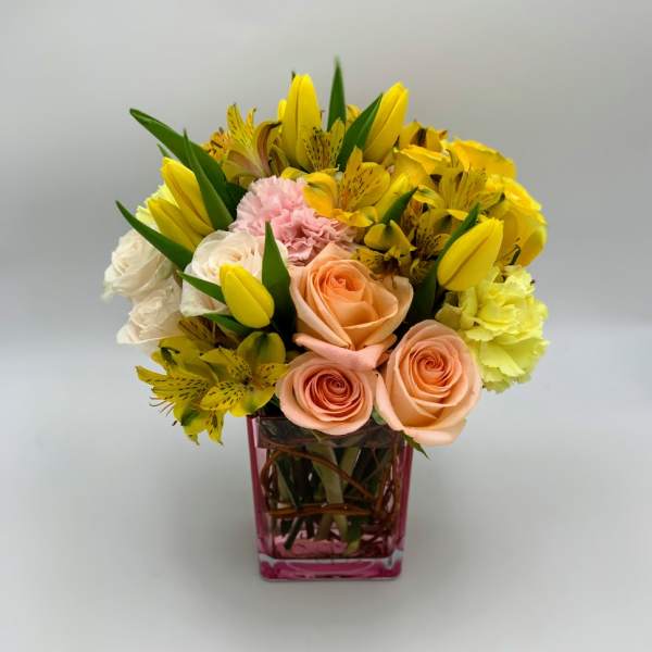 Bouquet of yellow lilies, peach roses, and pink carnations in a pink glass vase