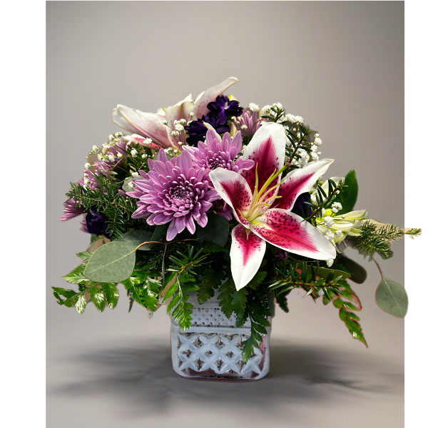 Pink lilies and lavender mums arranged with white filler flowers in a white cube vase