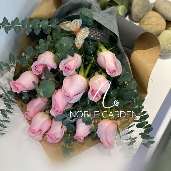 Bouquet of pale pink roses wrapped in dark paper with eucalyptus