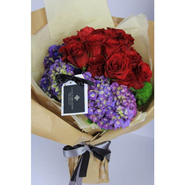 Bouquet of red roses and purple hydrangeas wrapped in brown paper