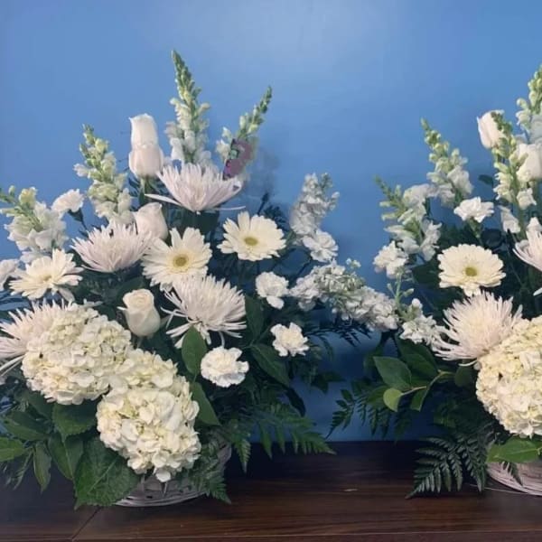 Two white floral arrangements in baskets with daisies and hydrangeas