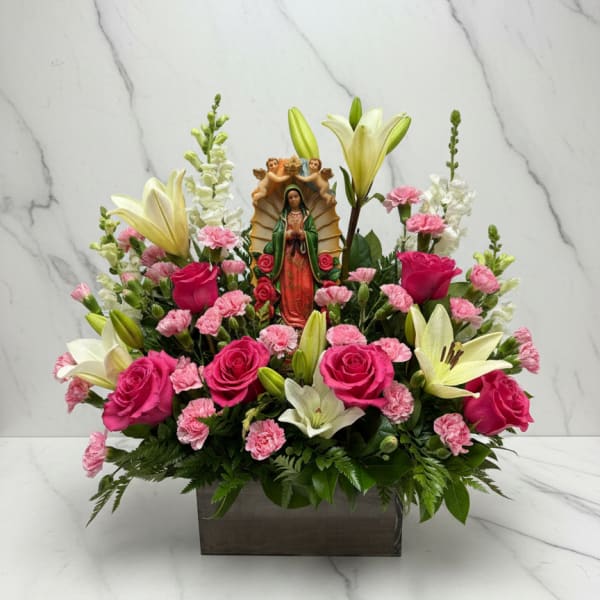 Pink roses and lilies arranged around a religious figurine in a rectangular vase
