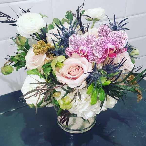 Bouquet of pink roses, white blooms, and spotted orchids in a glass vase