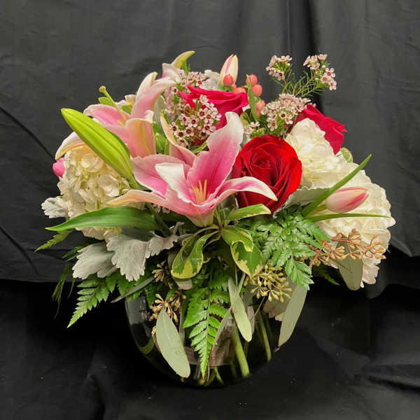 Bouquet of pink lilies, red roses, and white hydrangeas in a glass vase