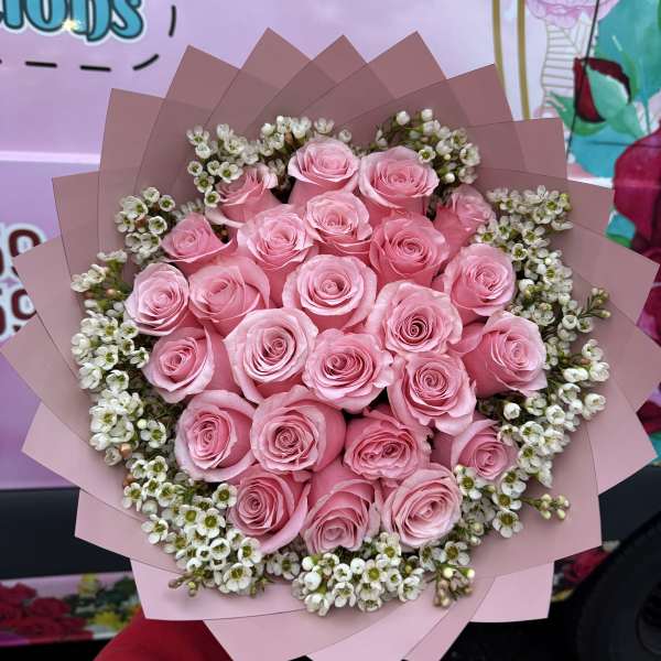 Bouquet of pink roses with small white filler flowers wrapped in pink paper