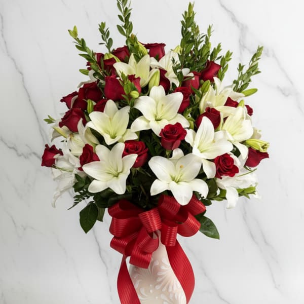 Red roses and white lilies arranged in a decorative vase with a red ribbon