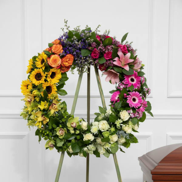 Colorful floral wreath on a standing easel beside a casket