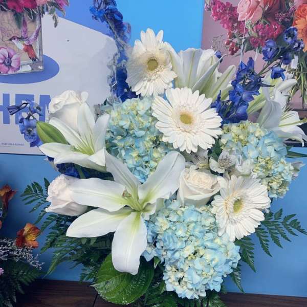 White lilies, gerbera daisies, and blue hydrangeas in a glass vase