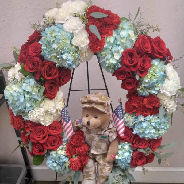 Heart-shaped floral wreath with roses, hydrangeas, and a teddy bear in military uniform